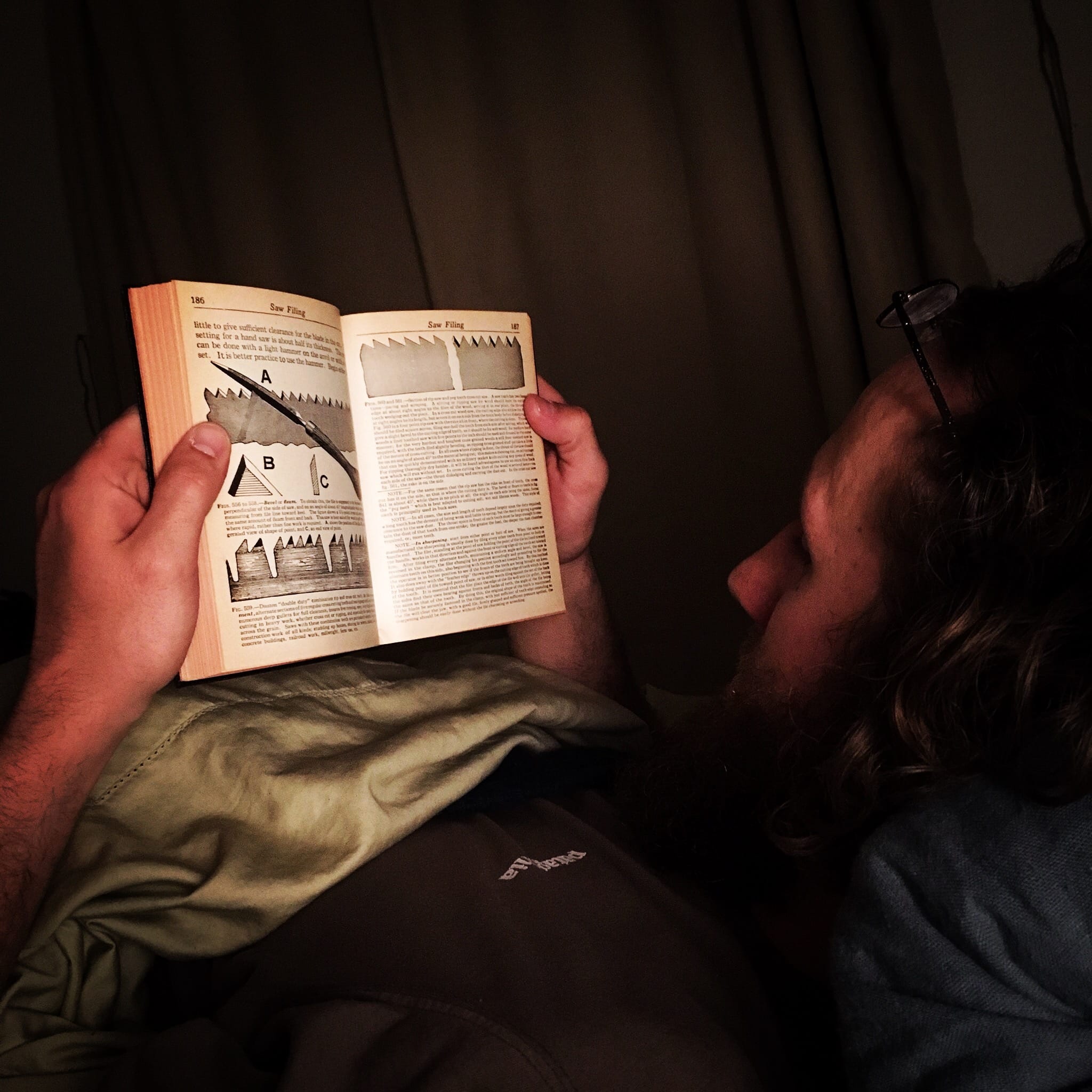 man reading about saw sharpening while in bed. Zach in About Maxon Made