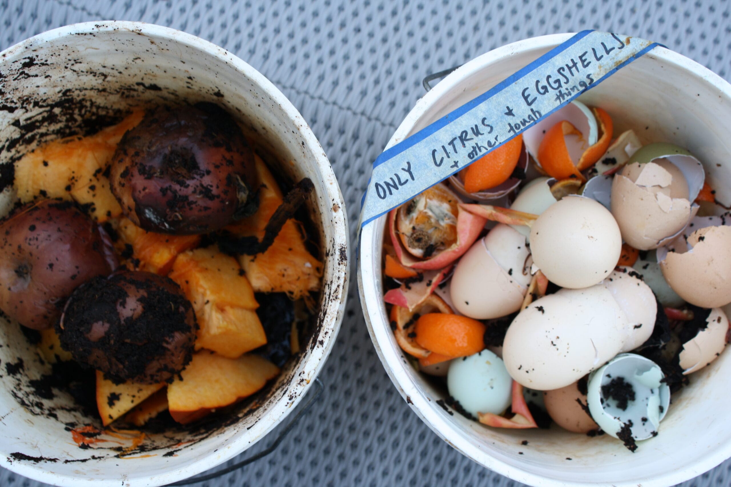 two buckets of food scraps from the kitchen. One has softer foods to the worms to eat. The other has a label that says "only citrus, eggshells and other tough things."