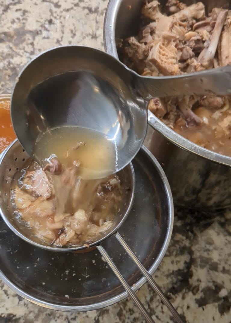 Ladling bone broth into jars through a strainer on the kitchen counter.