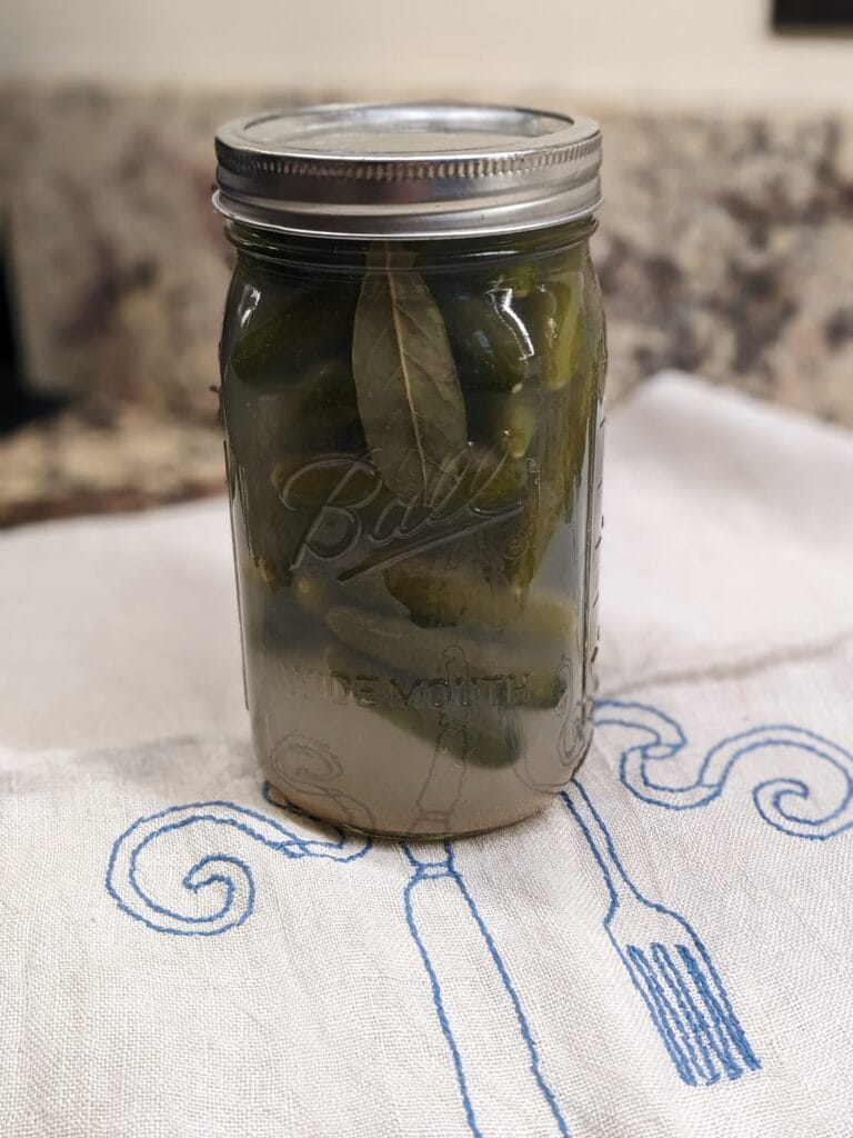A quart sized Maxon jar packed with mini cucumbers that have naturally fermented in a salt brine, sitting on a linen tea towel on the counter.
