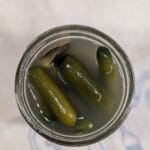 An open quart sized Maxon jar packed with mini cucumbers that have naturally fermented in a salt brine, sitting on a linen tea towel on the counter.