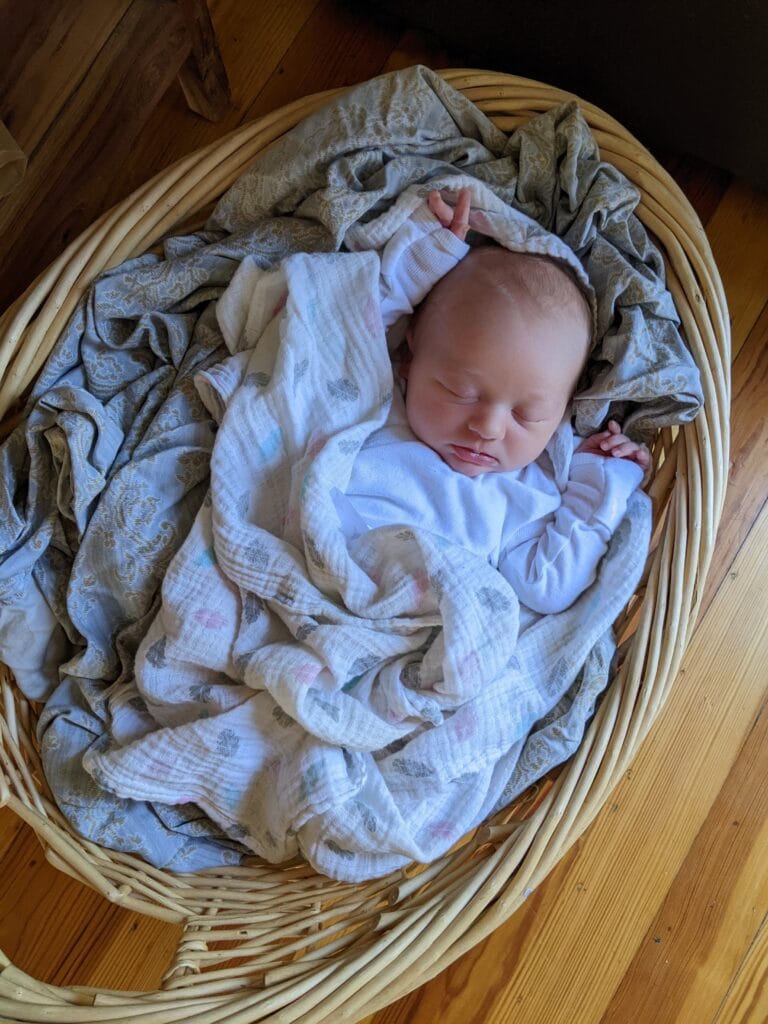 A sweet little baby sleeping on a pile of sheets in a wicker laundry basket - definitely inspiration for How To Stop Folding Your Kids' Laundry And What To Do Instead