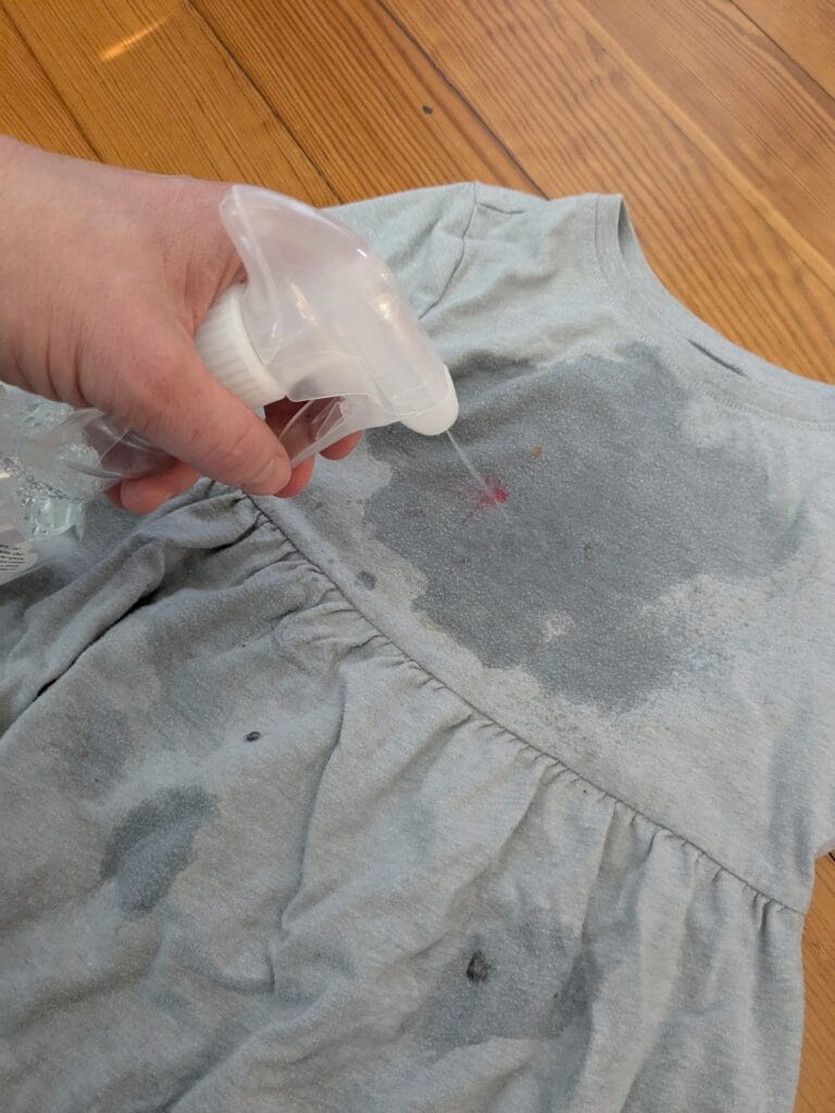 someone spraying a homemade natural stain treatment solution onto a stained child's dress