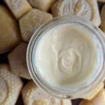 A small glass jar filled with the best homemade lotion you'll ever make. It's sitting on top of an array of molded beeswax shaped into hearts, hexagons and rectangles.