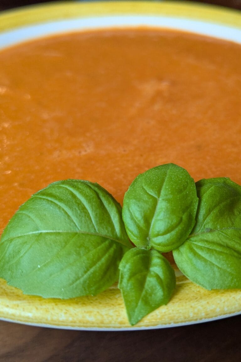 Yellow stripe bowl of tomato soup concentrate made into tomato soup by reconstituting with milk, garnished with fresh basil, resting on a wooden cutting board.