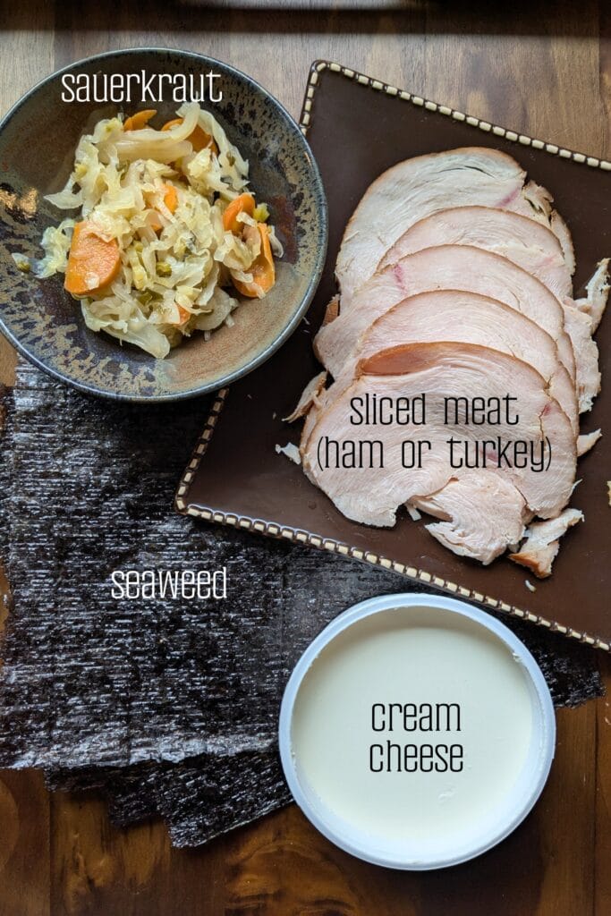 an arial view of all of the ingredients you'll need to make seaweed roll-ups with seaweed, cream cheese, sliced deli meat and sauerkraut