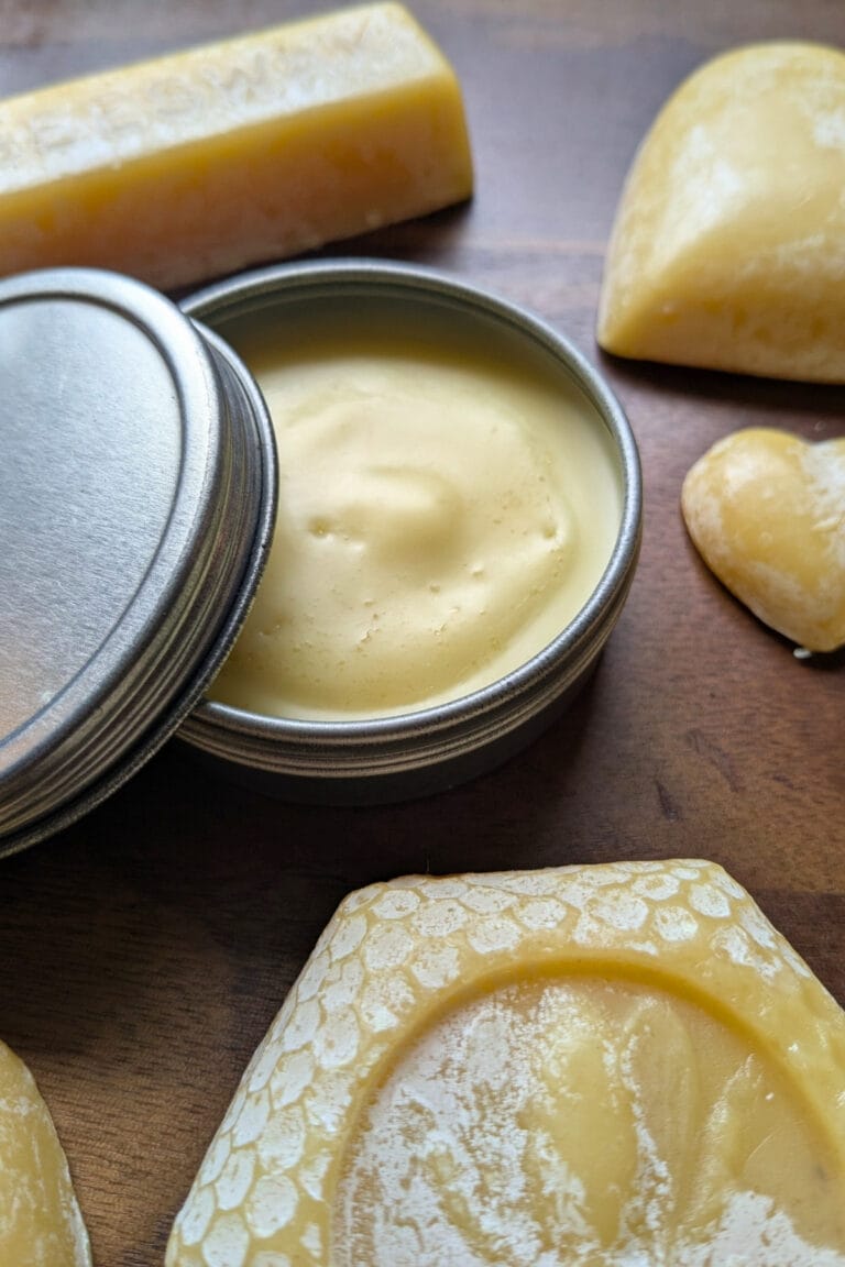 a tin of homemade honey hand balm surrounded by shaped beeswax molds