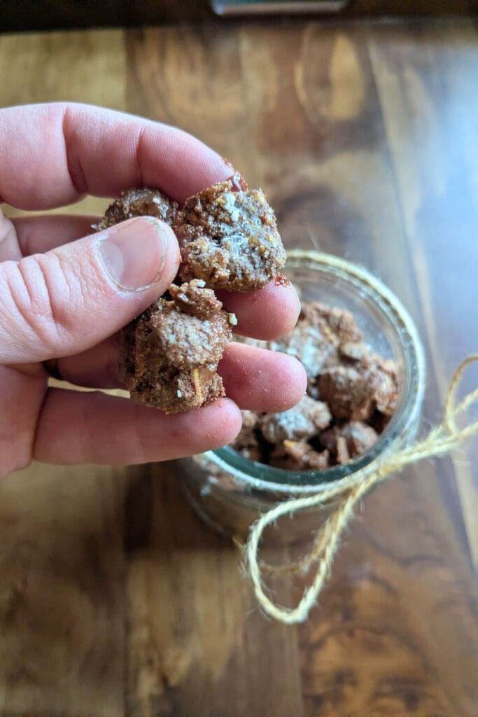 a hand holding freshly made, rich, gooey puppy chow with more protein, peanut butter, dark chocolate, pastured butter and collagen peptides, and a lot less powdered sugar!
