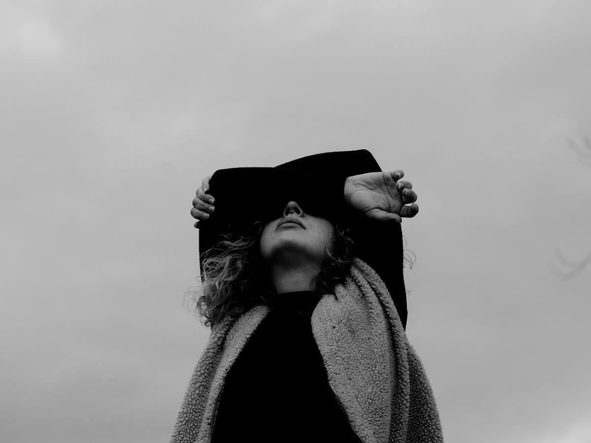 A woman in black  holding her folded arms against her face and looking up into the gray sky, representing Letting Fear Be Present Without Letting It Decide: One Important Reassurance - you are scared because it matters.