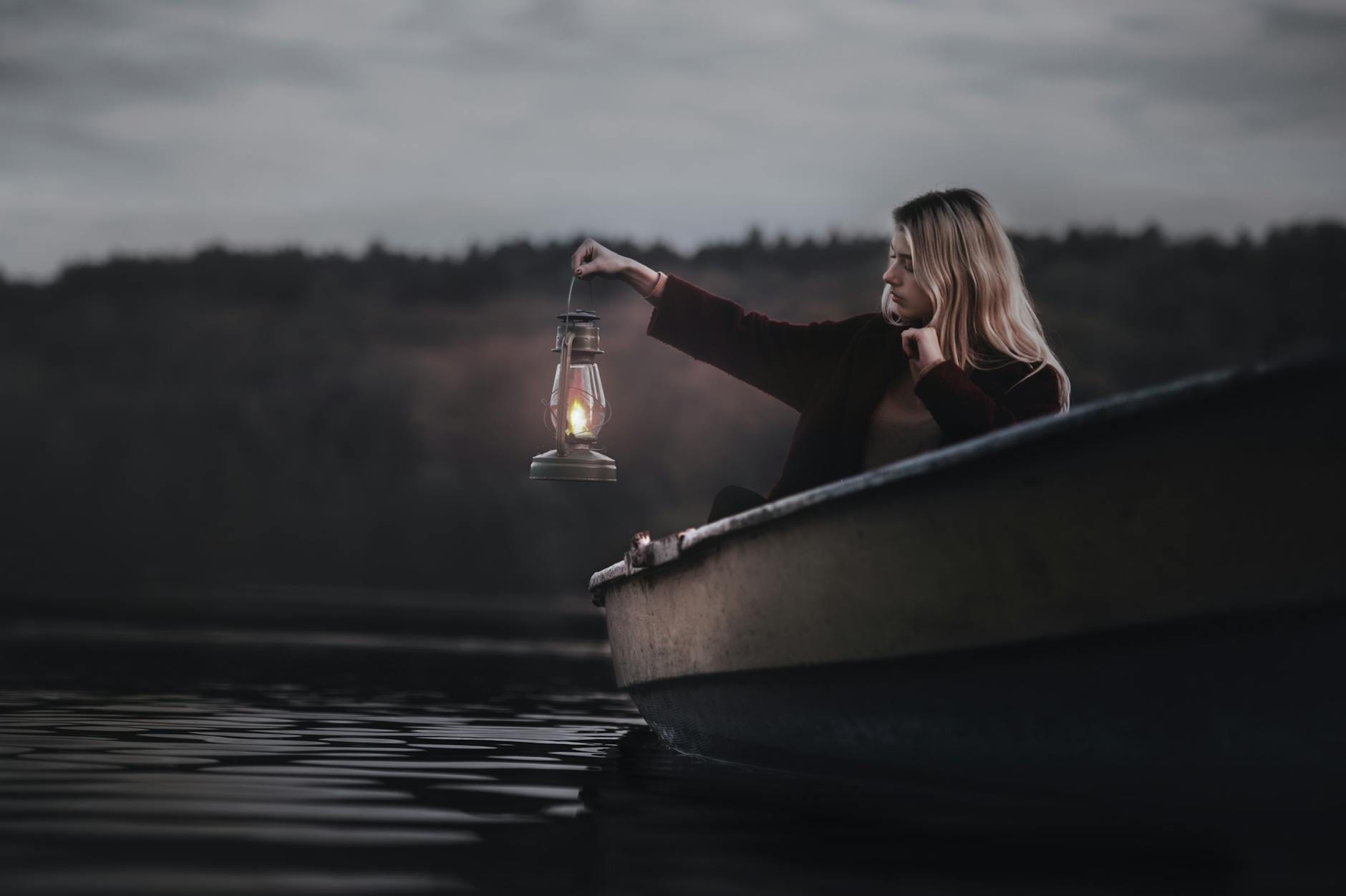 A woman in a row boat holding a lantern over the dark water, representing Calling In Another Baby Without Forcing the Outcome or overriding your fear.