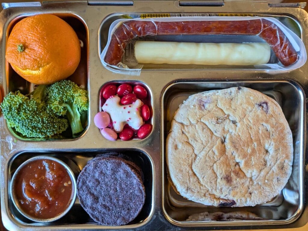 high protein school lunch example with meat stick, cheese stick, cream cheese and jelly sandwich, fruits, veggies and a sweet treat
