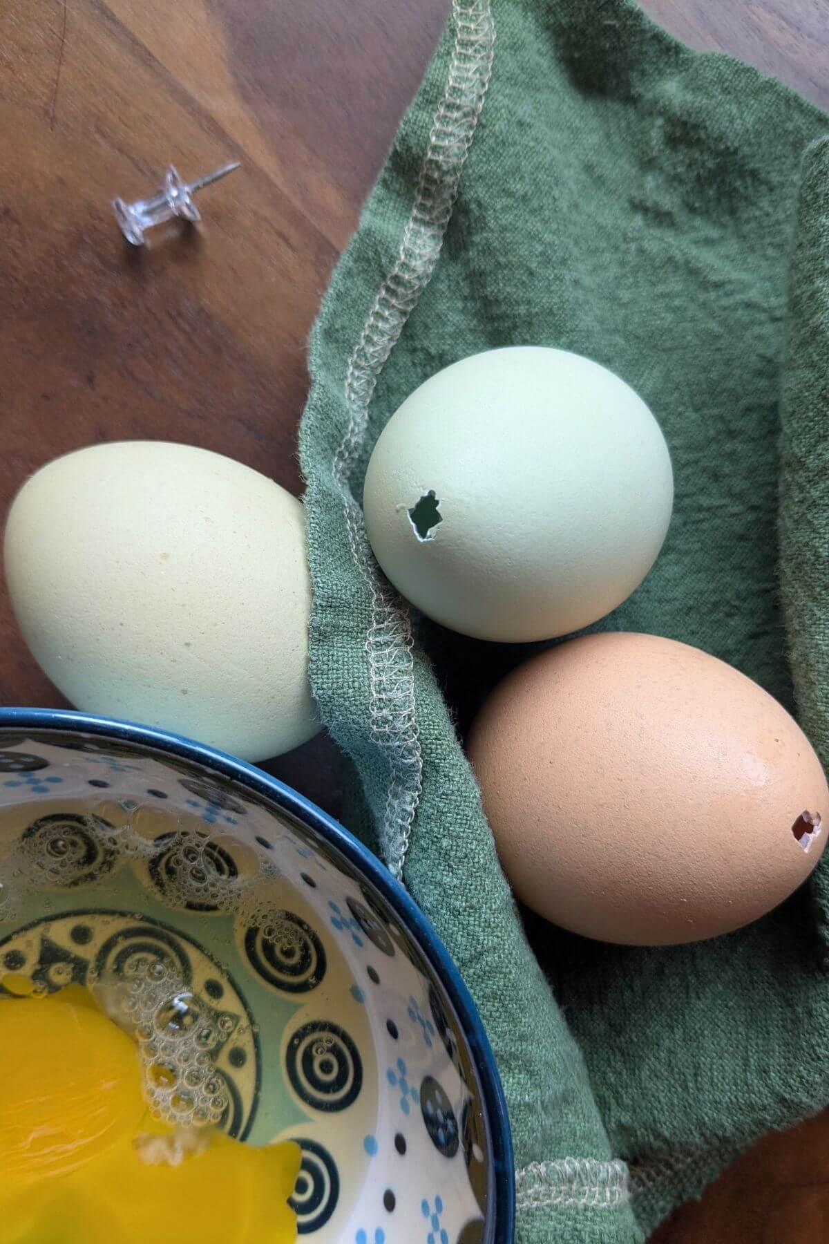 Neutral toned decorated eggs on a linen napkin prepared by blowing out eggs using an easy no-mouth method. Egg white and yolk are in a nearby bowl.
