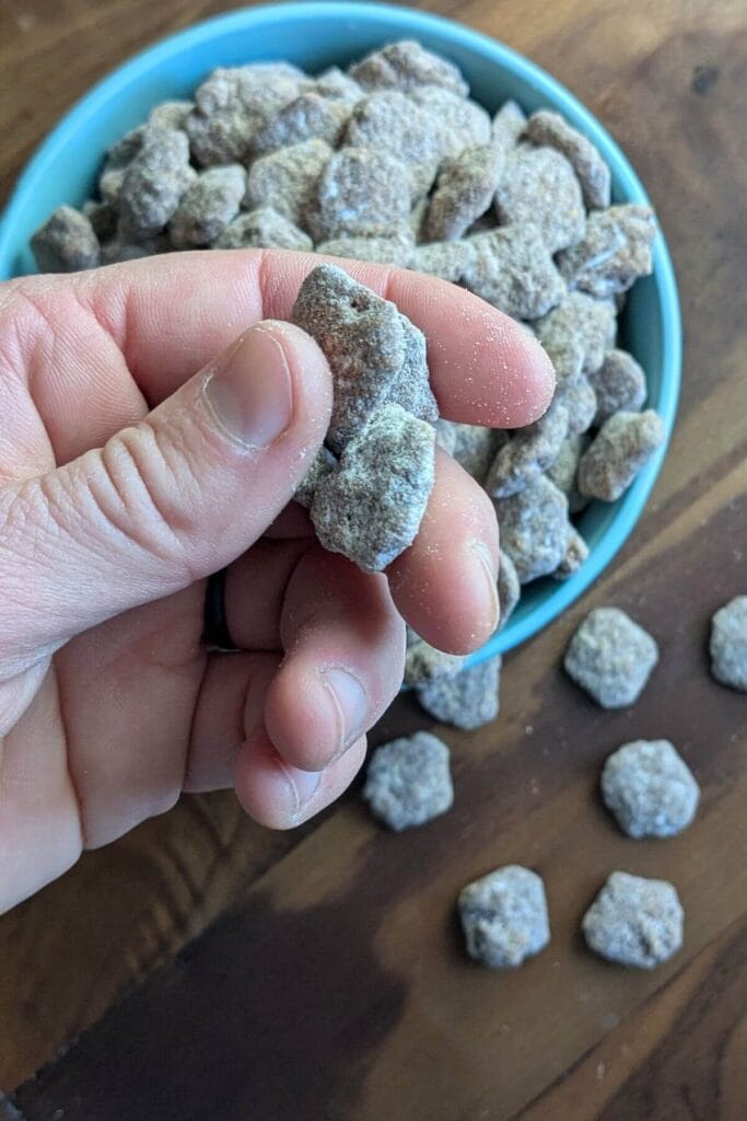 a hand holding freshly made, rich, gooey puppy chow with more protein, peanut butter, dark chocolate, pastured butter and collagen peptides, and a lot less powdered sugar!
