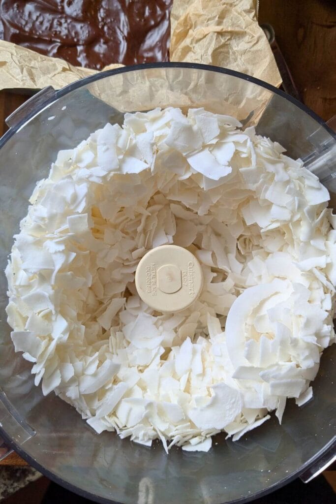 large coconut flakes in a food processor ready to finely shred