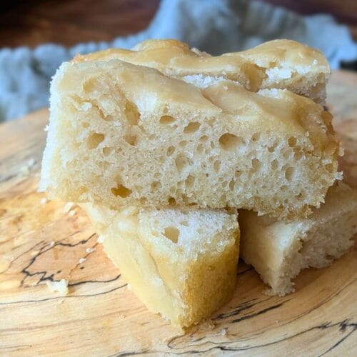 This easy sourdough focaccia starts with unfed starter straight from the fridge and can be baked the same day. Here are pieces sliced up on a cutting board for eating.