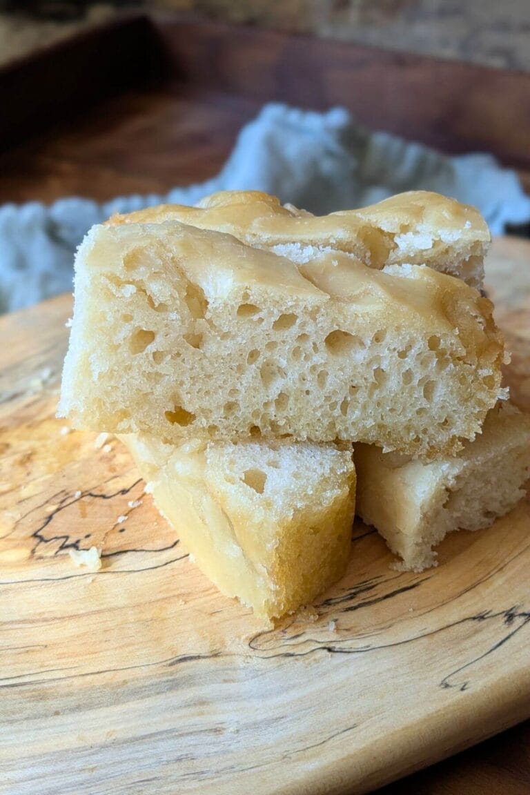 This easy sourdough focaccia starts with unfed starter straight from the fridge and can be baked the same day. Here are pieces sliced up on a cutting board for eating.