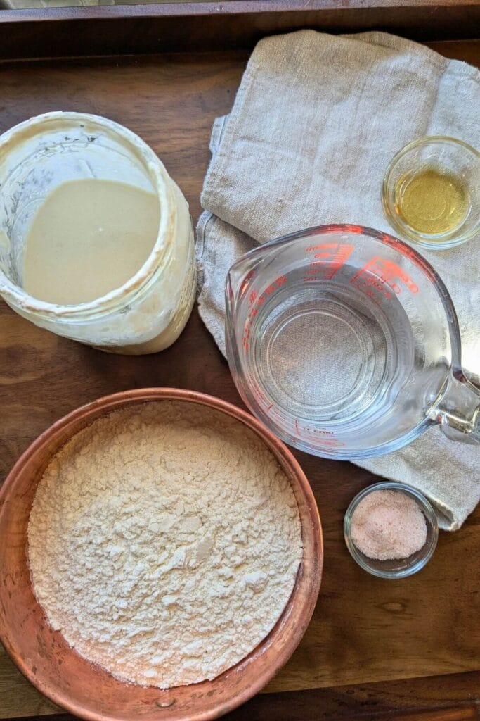 ingredients measured out for a sourdough focaccia: flour, water, cold sourdough starter from the fridge, honey and sea salt