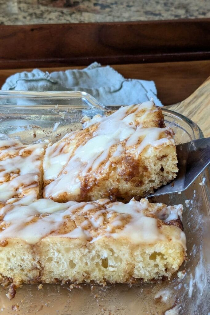 Easy, no knead, same-day sourdough cinnamon roll focaccia drizzled with cream cheese frosting and cut to serve