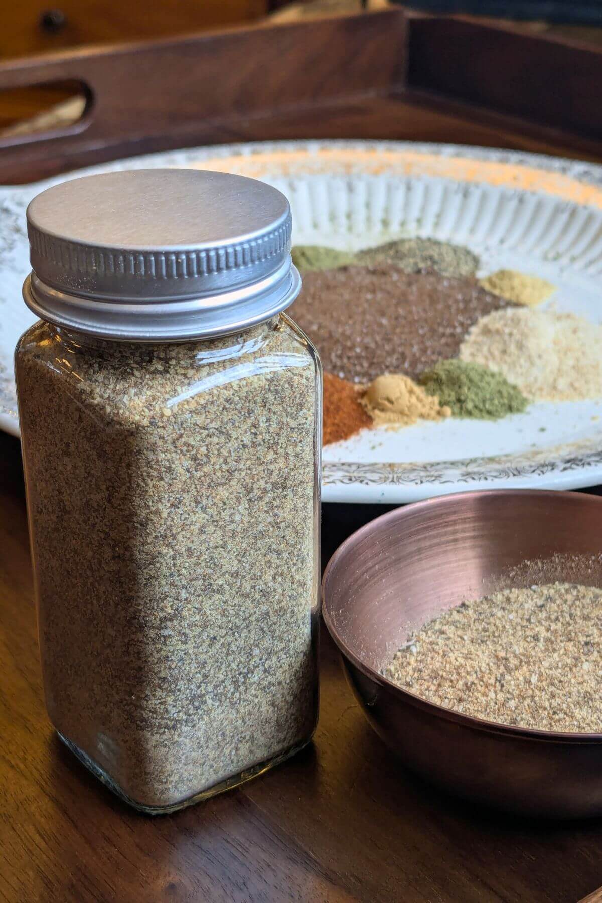 Ingredients for homemade chophouse seasoning including smoked salt, garlic, herbs and spices and Homemade chophouse seasoning in a glass jar beside them.