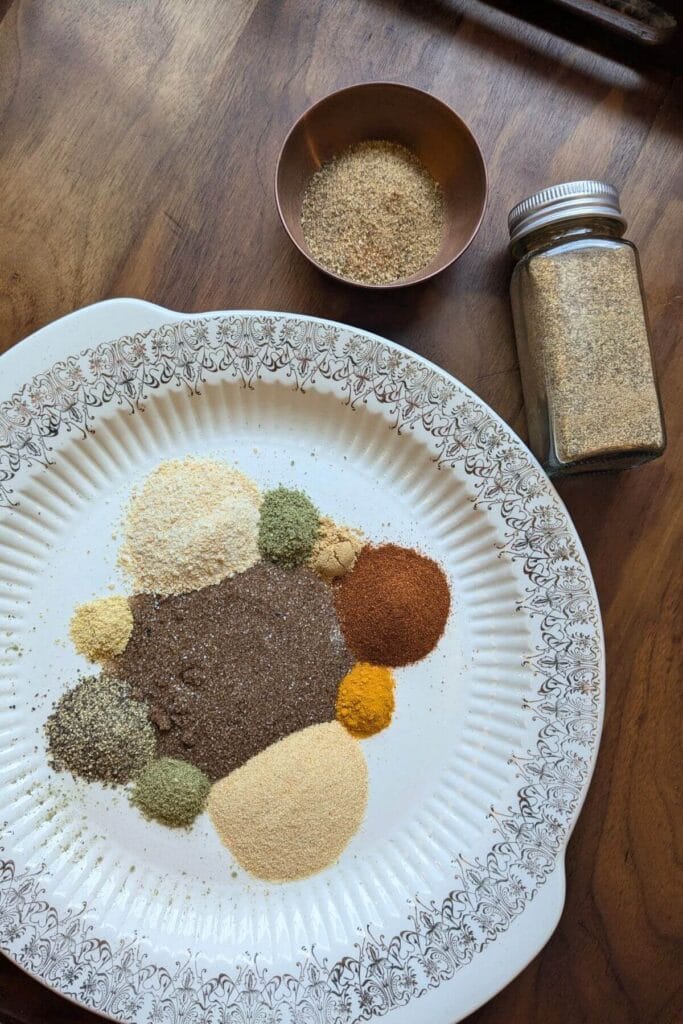 Ingredients for homemade chophouse seasoning arranged with smoked salt, garlic, onion, herbs, paprika, ginger, turmeric, mustard and spices.