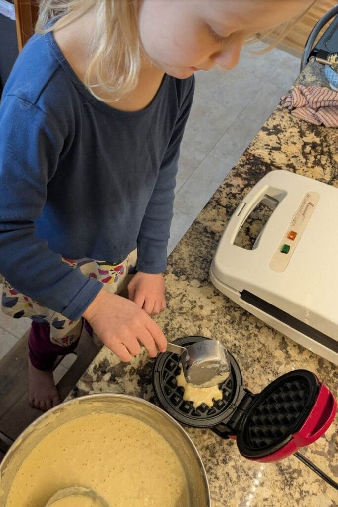 a small child chef using a mini waffle iron to make sourdough protein waffles