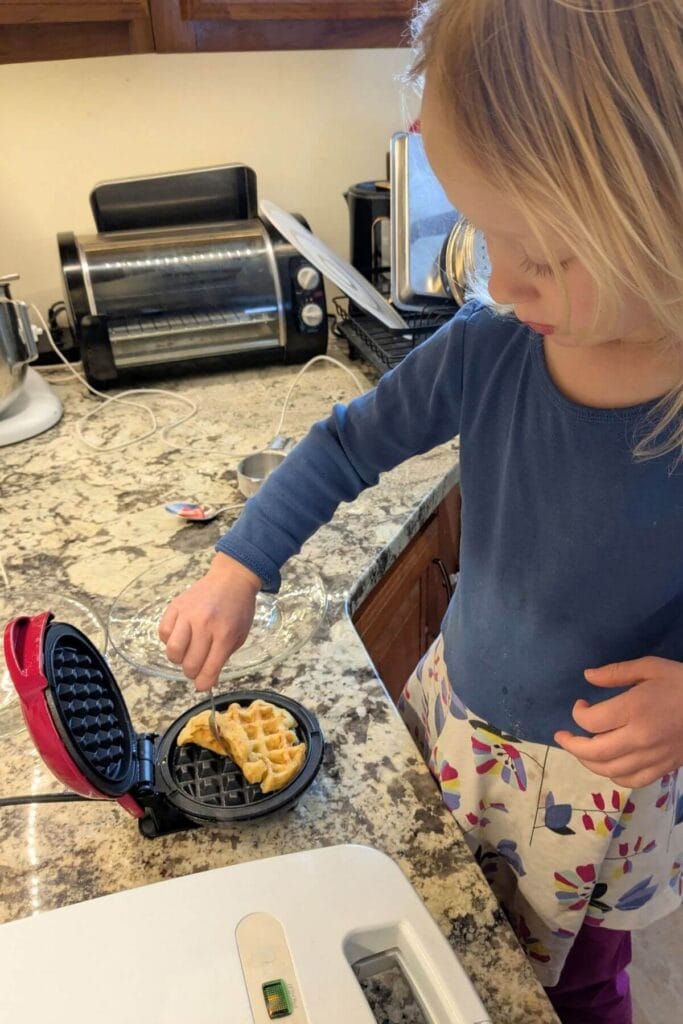 a small child chef using a mini waffle iron to make sourdough protein waffles